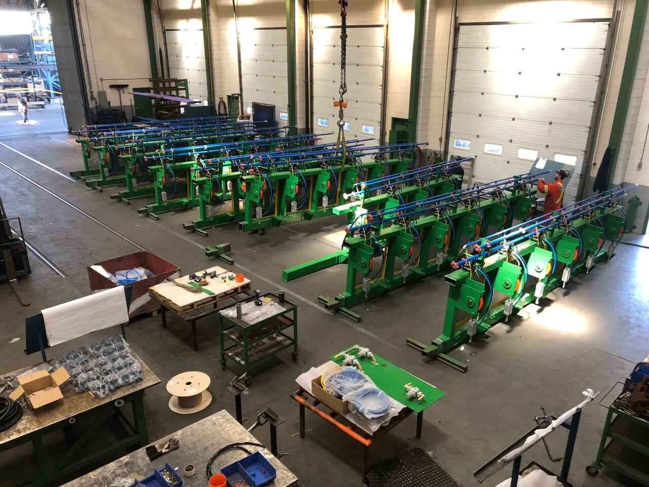Industrial warehouse interior with multiple green machines lined up, workstations with tools and materials, and a worker inspecting equipment. Industrial warehouse interior with multiple green machines lined up, workstations with tools and materials, and a worker inspecting equipment.